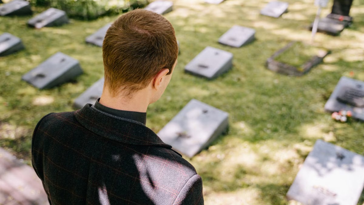 A man stands in contemplation at a serene memorial park surrounded by tombstones.
