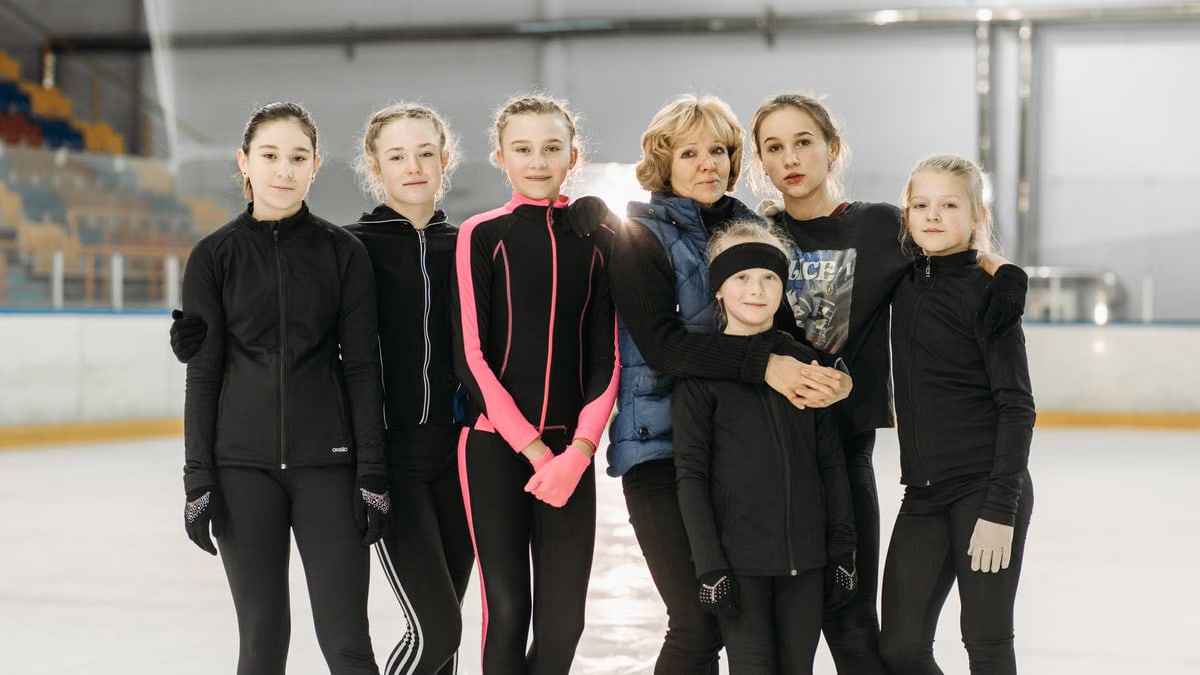 Close-up of young female ice skaters posing with their coach on an indoor rink.